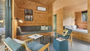A wooden cabin interior with a sofa, chairs, a coffee table, and a bed. - Modern holiday home near Dueodde Beach (Nexø)