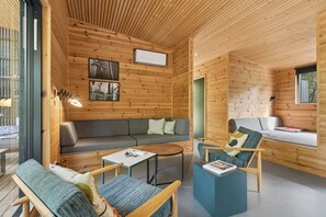 Ein Holzblockhaus-Interieur mit einer Couch, Sesseln, einem Couchtisch und einem Bett.