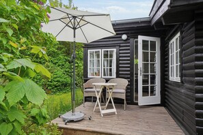 En træterrasse med et bord, stole og en parasol, samt en dør til et værelse.