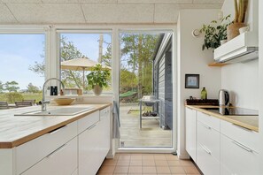 A modern kitchen with an open door leading to a deck, a sink, a stove, and a plant on the counter. - Cozy low-energy home with sea views (Ørsted)