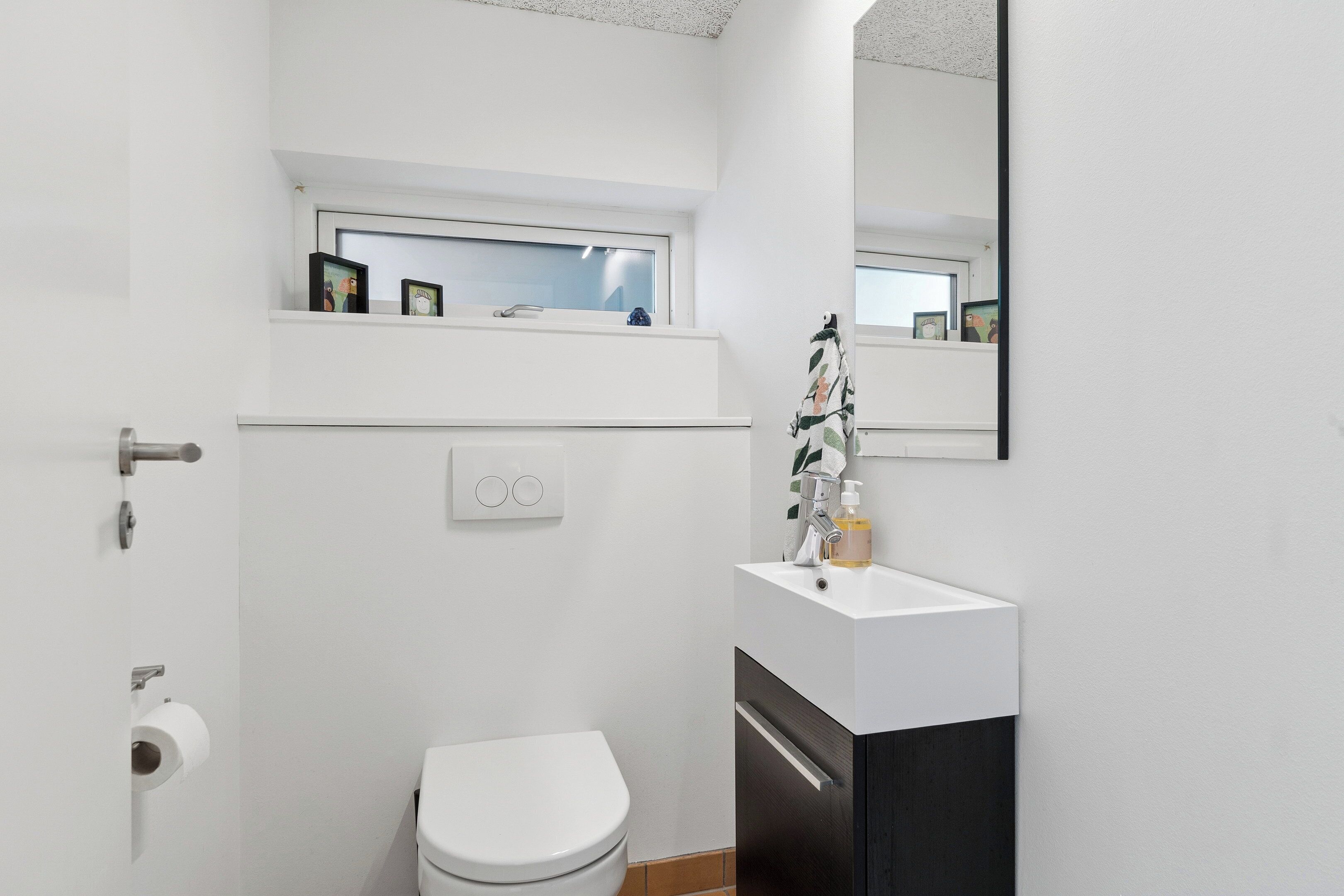 A modern bathroom with a toilet, a sink, a mirror, and a window above the sink.