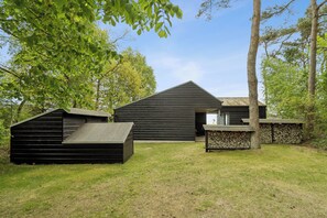 A modern wooden cabin with a sloped roof, a small deck, and a stone wall. - Cozy low-energy home with sea views (Ørsted)