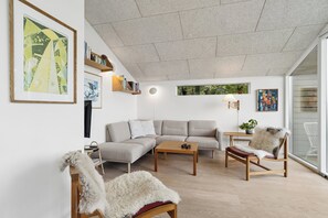 A modern living room with a sofa, coffee table, and chairs, a bookshelf, and artwork on the walls. - Cozy low-energy home with sea views (Ørsted)