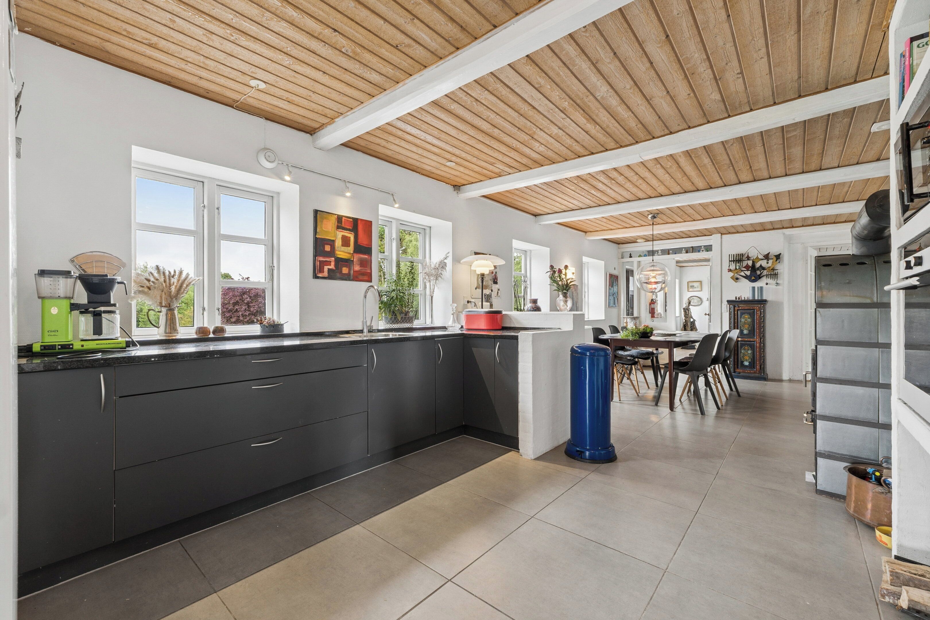 A modern kitchen with a wooden ceiling, black cabinets, and a dining area with chairs and a table.