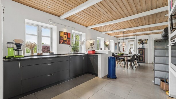 A modern kitchen with a wooden ceiling, black cabinets, and a dining area with chairs and a table. - Large charming house for 12 guests (Snøde)