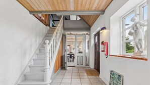 A staircase with white balusters, a wooden ceiling, and a tiled floor leading to a door. - Large charming house for 12 guests (Snøde)