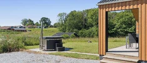 A wooden pavilion with a gravel path leading to it, surrounded by greenery and a clear sky.