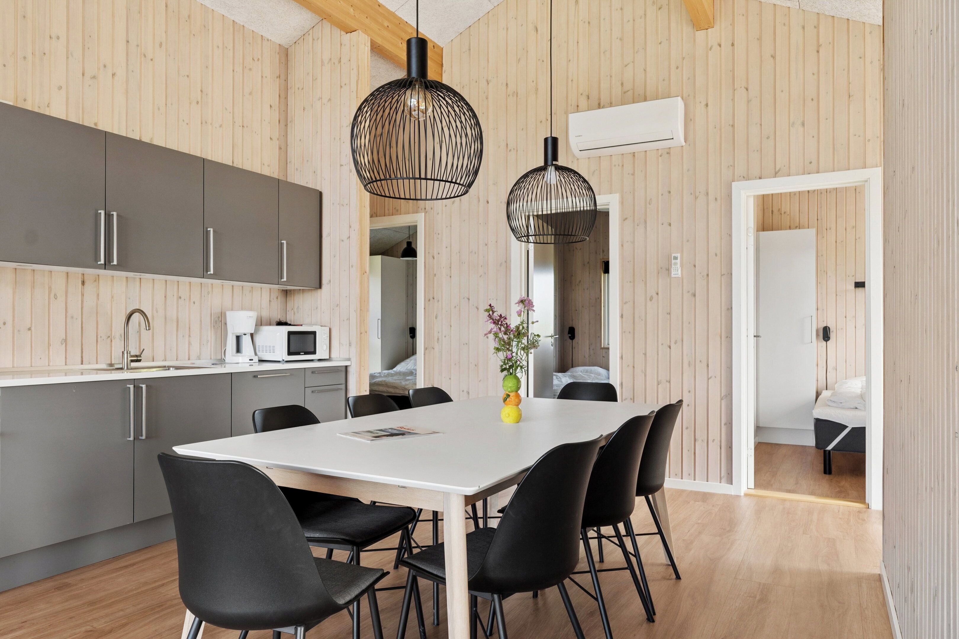 Una cocina moderna con armarios grises, una encimera blanca y un comedor con mesa blanca y sillas negras.