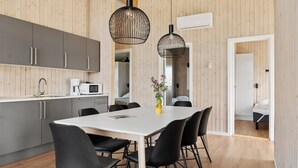 Une cuisine moderne avec des meubles gris, un plan de travail blanc et un coin repas comprenant une table blanche et des chaises noires.