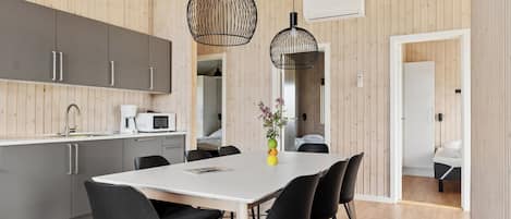 Una cocina moderna con armarios grises, una encimera blanca y un comedor con mesa blanca y sillas negras.