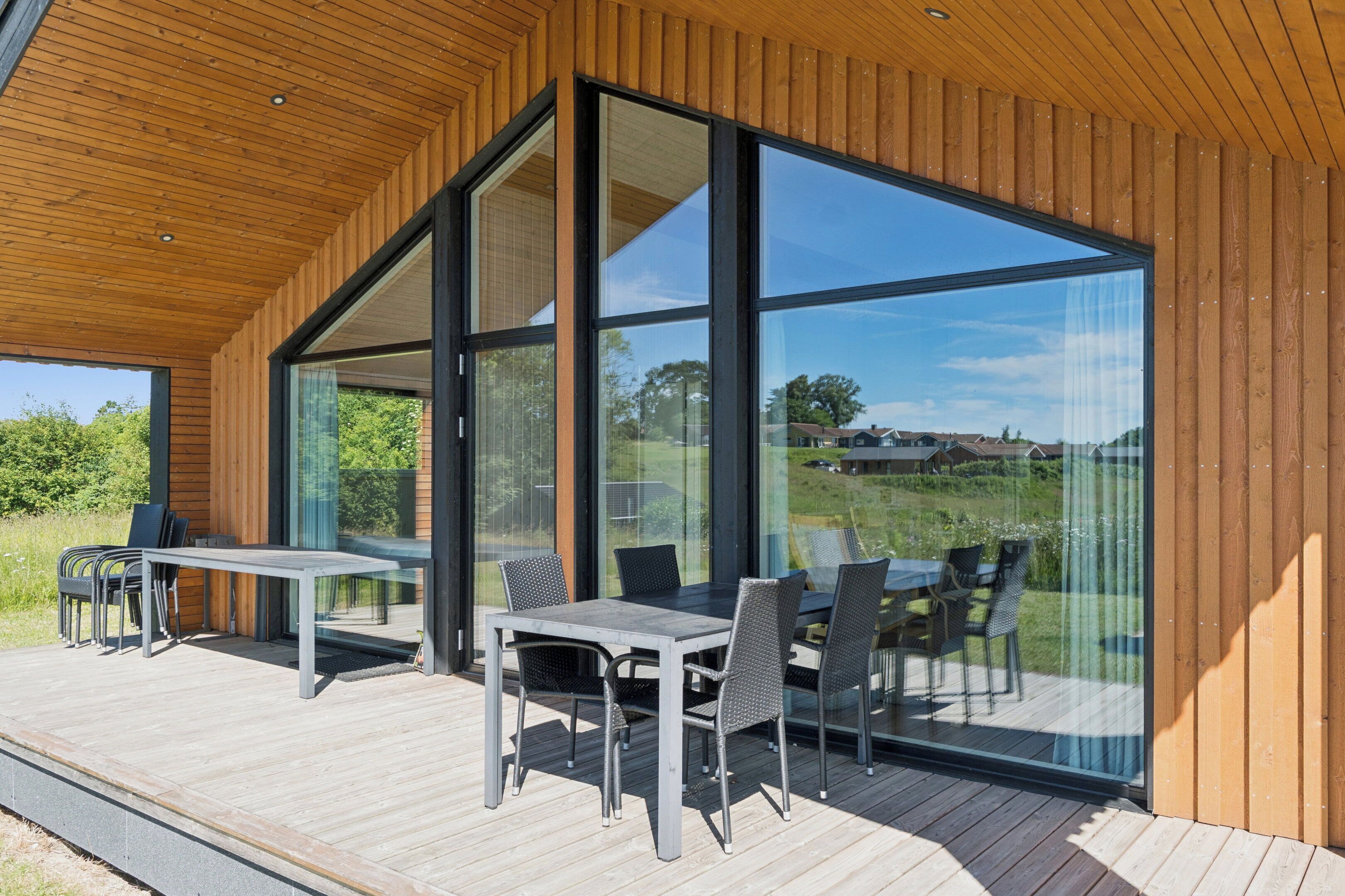 A modern outdoor dining area with a wooden deck, glass walls, and a clear view of the surrounding landscape.