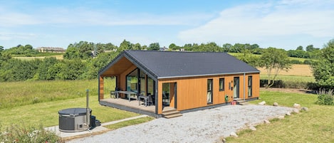 A modern wooden cabin with a deck, a fireplace, and a gravel driveway.