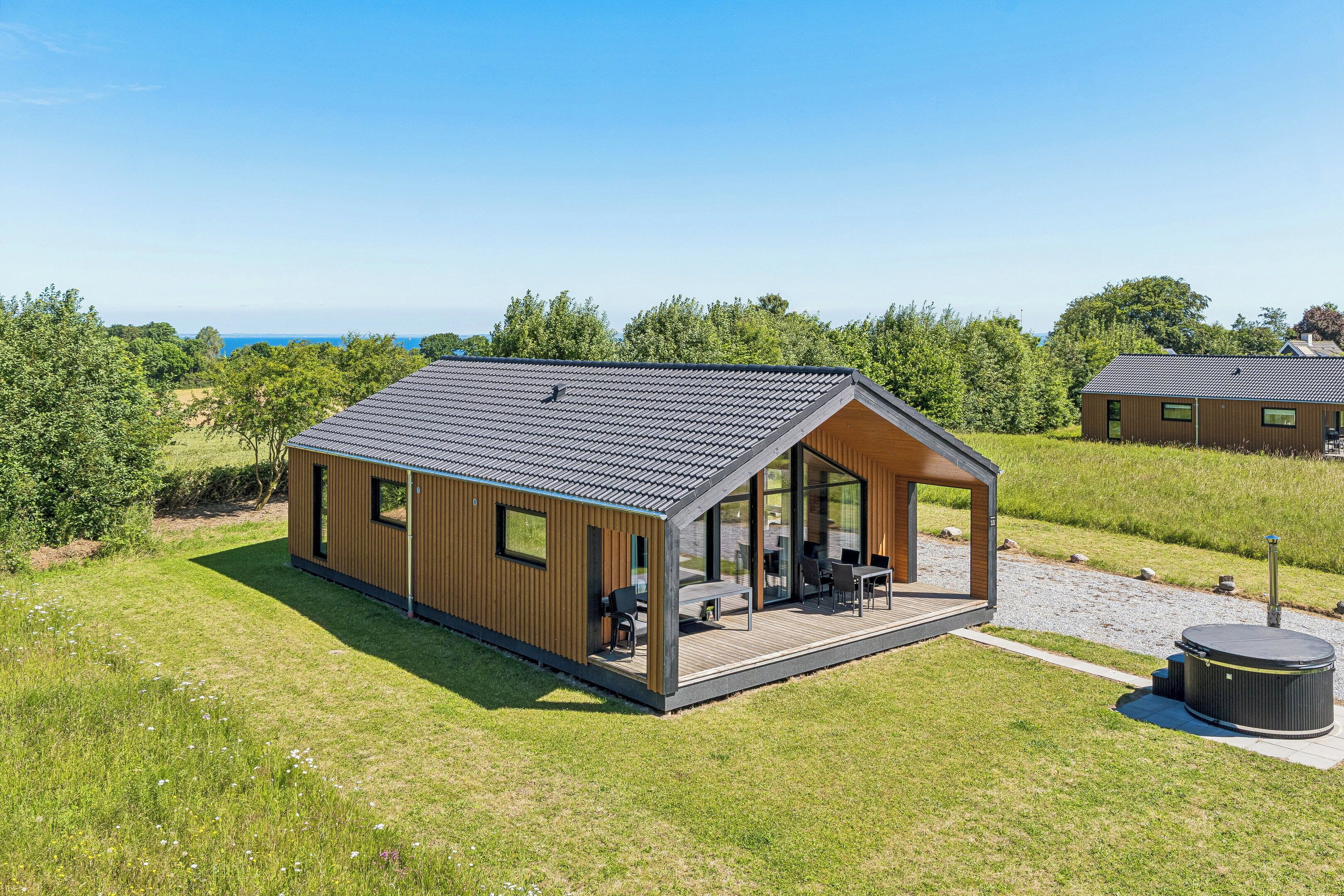 Une cabane moderne en bois, dotée d’un patio couvert, de grandes fenêtres et offrant une vue sur la mer.