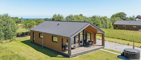Une cabane moderne en bois, dotée d’un patio couvert, de grandes fenêtres et offrant une vue sur la mer.