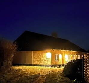A house with a stone facade, a dark roof, and a well-lit front porch. - Idyllic Old Cottage, with low ceilings (Bredebro)