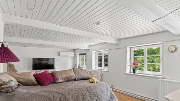 A bedroom with a bed, a TV, a window with a view, and a radiator. - Idyllic Old Cottage, with low ceilings (Bredebro)