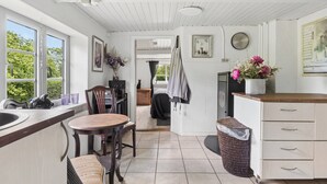 A kitchen with a wooden countertop, a sink, a dining table with chairs, a wicker waste basket, and a view of the garden through the window. - Idyllic Old Cottage, with low ceilings (Bredebro)