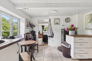 Eine Küche mit Holzarbeitsplatte, einem Spülbecken, einem Esstisch mit Stühlen, einem Korbwäschesammler und Blick auf den Garten durch das Fenster.