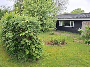 Ein kleines schwarzes Haus mit Fenster und Tür, umgeben von einem grasbewachsenen Hof und dichtem Grün.