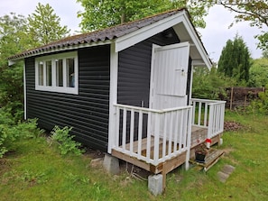 Eine kleine, dunkle Holzhütte mit einer weißen Tür und einer Veranda.