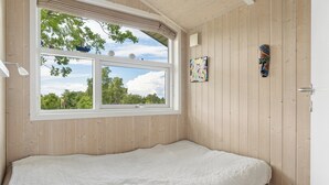Huone, jossa on sänky, ikkuna, josta avautuu näkymä puihin, ja seinälle ripustettu taideteos.