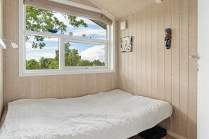Ein Zimmer mit einem Bett, einem Fenster mit Blick auf Bäume und einem an der Wand befestigten Kunstwerk.