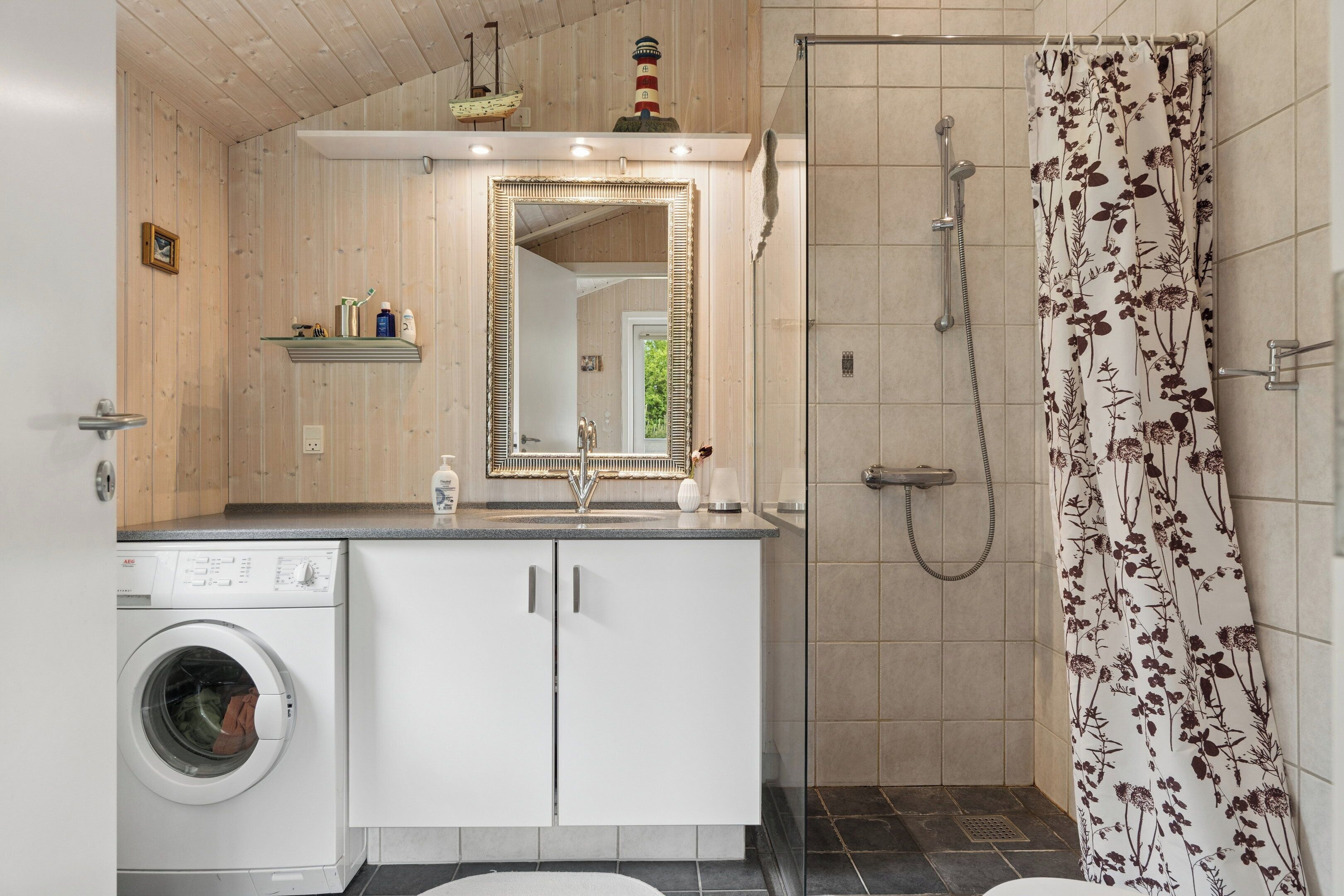 Een badkamer met een wasmachine, een spiegel, een douche en een douchegordijn met bloemenprint.