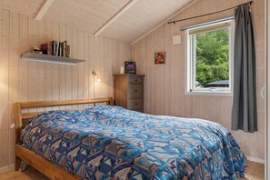 Ein Schlafzimmer mit einem hölzernen Bett, einem Fenster mit Blick auf Bäume, einem Bücherregal und einer kleinen Kommode.