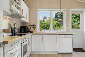 Eine moderne Küche mit weißen Schränken, einer Holz Arbeitsplatte, einem eingebauten Geschirrspüler und einem Fenster mit Blick auf Grünflächen.