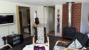 A living room with a TV, a guitar, a fireplace, and a dining area with a table and chairs. - Cottage on the island IVÖ in Skåne (Fjälkinge)