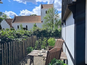 A wooden table with chairs, a white building with a red-tiled roof, and a wooden fence in a garden setting.