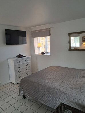 Un dormitorio con cama, cómoda, televisor, ventana con lámpara y espejo.