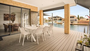 A modern outdoor dining area with a wooden deck, a glass partition, and a view of the water and buildings. - Waterfront Halls Head Retreat – Sleeps 8, Spa & Home Theatre (Halls Head)