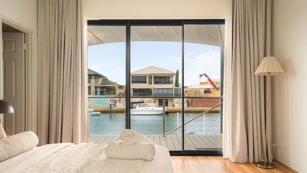 A bedroom with a large bed, a view of a marina, and a balcony with curtains. - Waterfront Halls Head Retreat – Sleeps 8, Spa & Home Theatre (Halls Head)