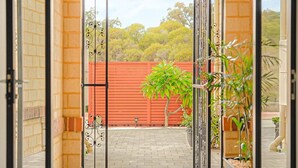 An open glass door leading to a paved area with a brick wall and a red fence in the background. - Waterfront Halls Head Retreat – Sleeps 8, Spa & Home Theatre (Halls Head)