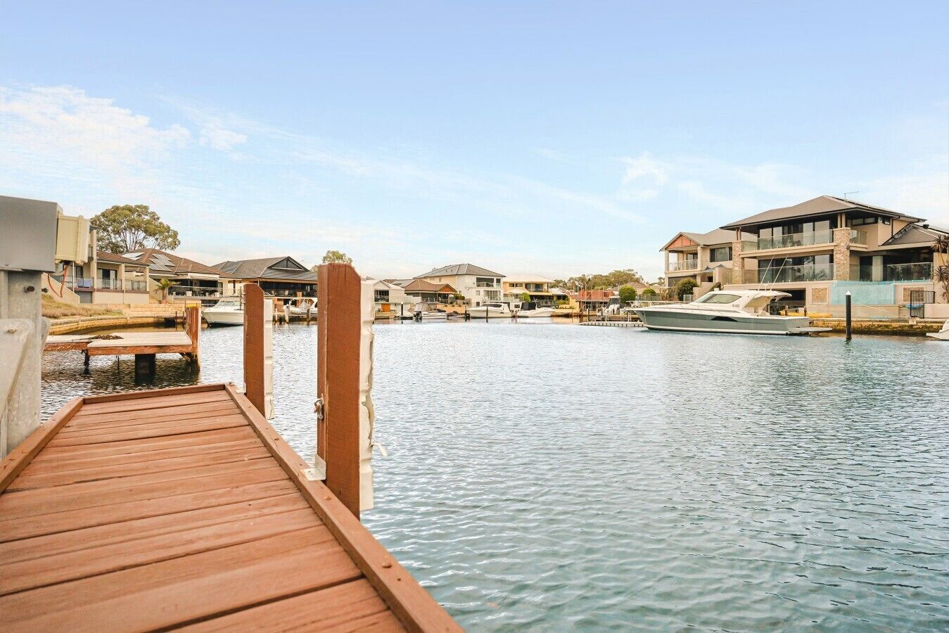 A wooden dock extending into calm water, surrounded by residential buildings with balconies and large windows.