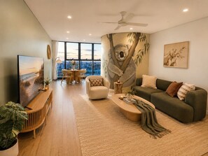 Uma sala de estar moderna com uma janela grande, um ventilador de teto, um sofá, uma mesa de centro e uma televisão.