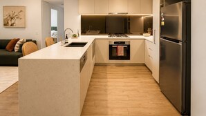 Een moderne keuken met een centraal eiland, een ingebouwde oven, een roestvrijstalen koelkast en houten vloeren.