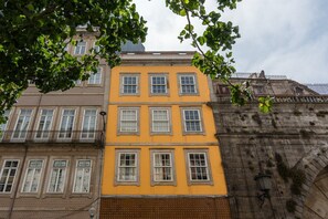 A multi-story building with a yellow facade, multiple windows, and a stone structure to the right.