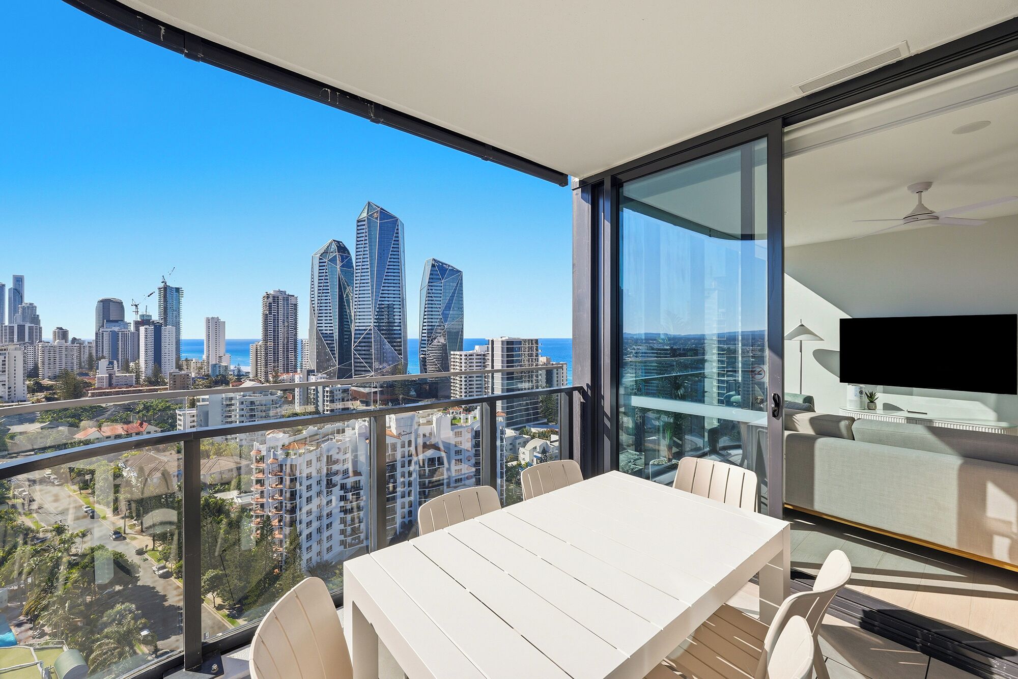 Un balcón con mesa y sillas, con vista a un paisaje urbano con edificios modernos y cielo despejado.