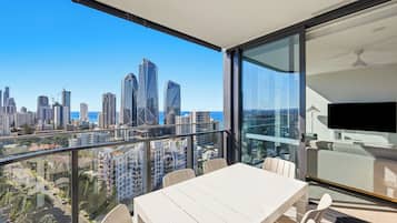 Un balcón con mesa y sillas, con vista a un paisaje urbano con edificios modernos y cielo despejado.