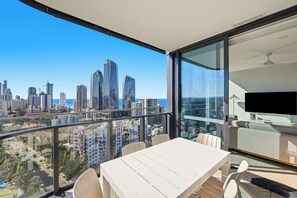A balcony with a table and chairs, overlooking a cityscape with modern buildings and a clear sky.
