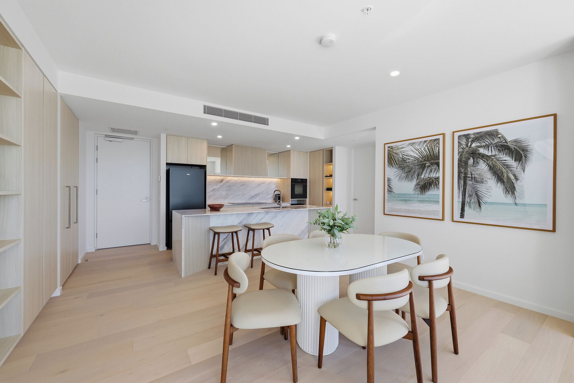 A modern kitchen with a central island, a dining area with a round table and chairs, and two framed pictures on the wall.