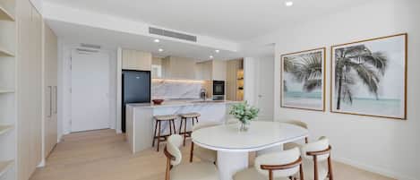 A modern kitchen with a central island, a dining area with a round table and chairs, and two framed pictures on the wall.
