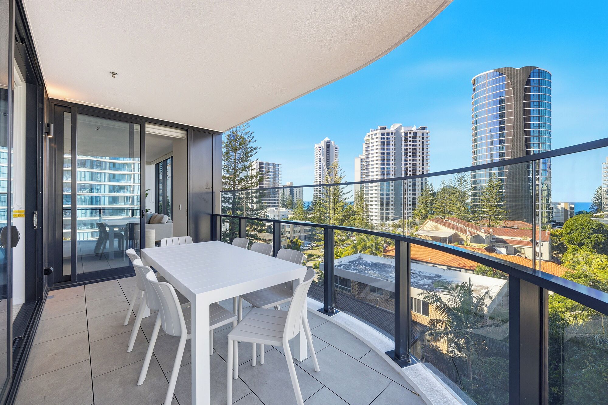 A balcony with a table and chairs, overlooking a cityscape with tall buildings.