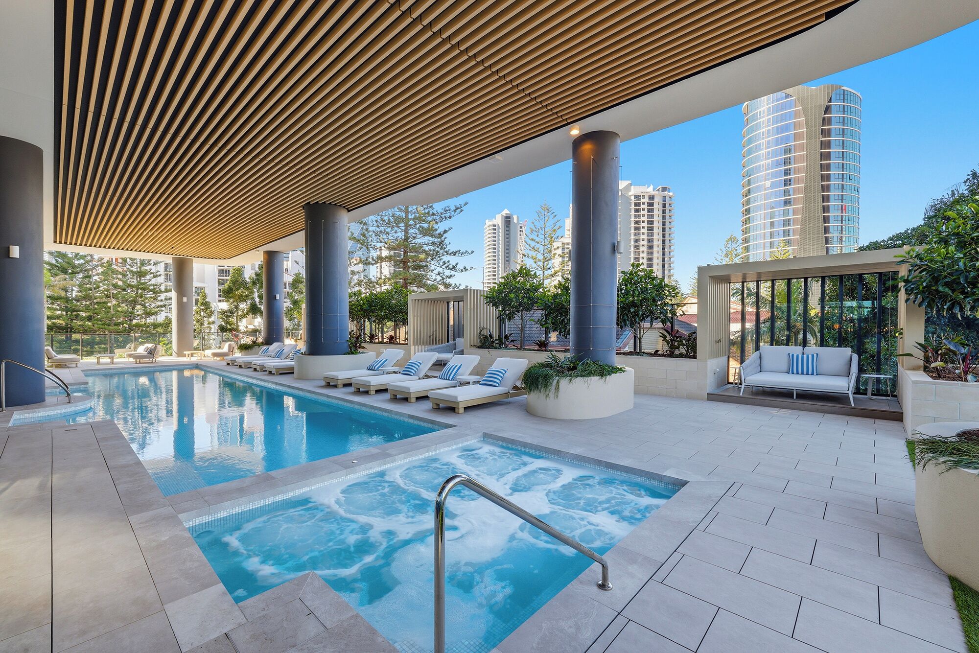 Un área de piscina en la azotea con sillones de descanso, un jacuzzi y vistas de edificios altos circundantes.