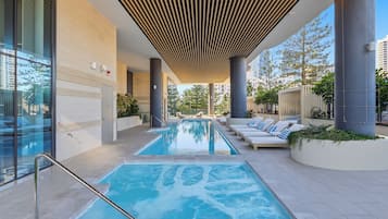 Uma área interna de piscina moderna, com piscina translúcida, espreguiçadeiras e teto com design de ripas exclusivo.