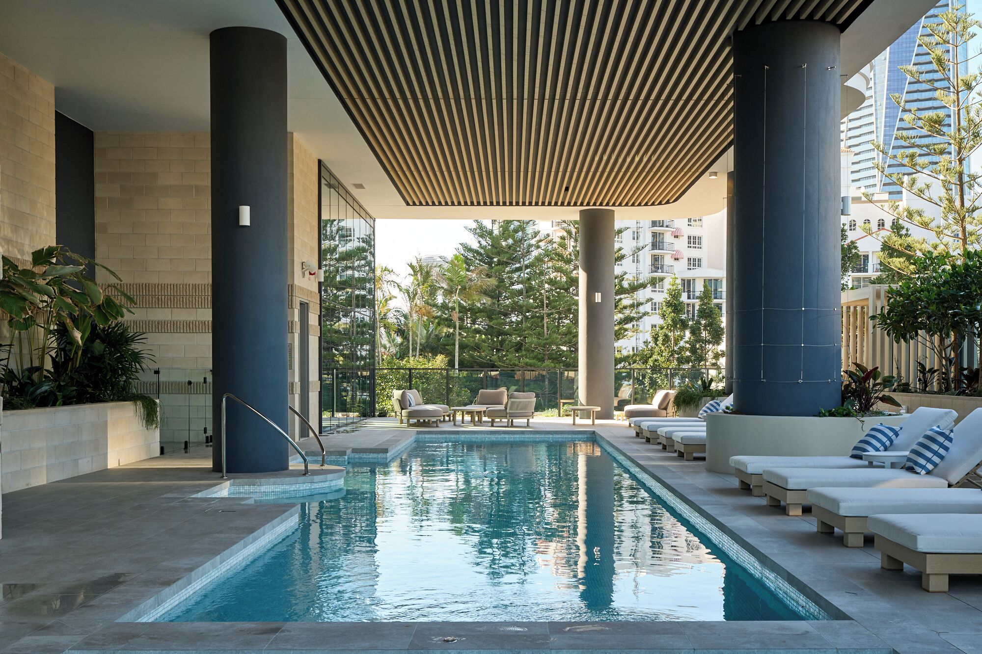 Piscina con sillas de descanso y una zona cubierta con columnas.