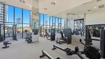 Uma academia moderna com diversos equipamentos de exercício, grandes janelas e vista para a paisagem urbana.