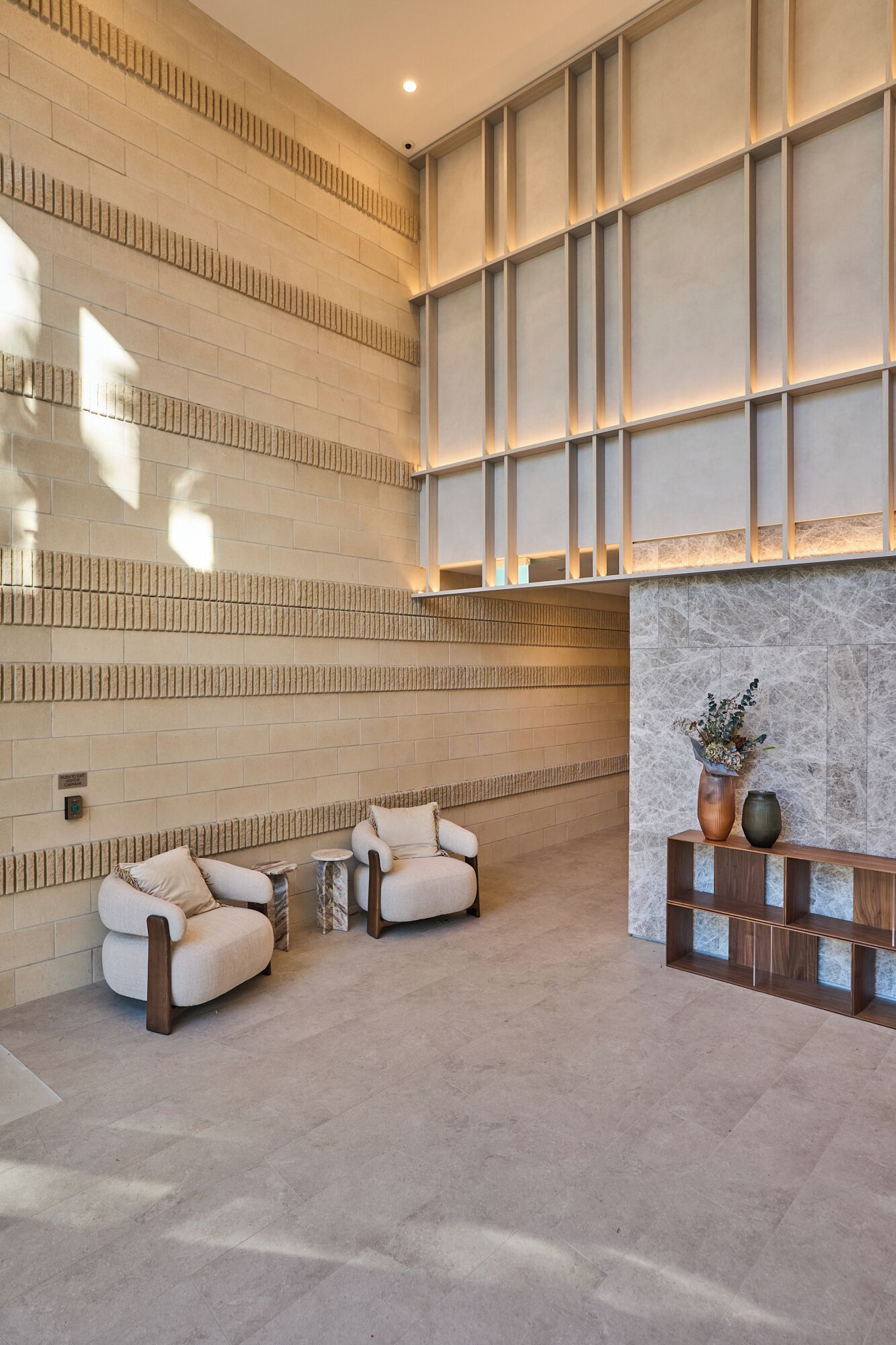 A lobby with a high ceiling, a marble fireplace, and two armchairs.